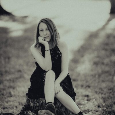 A black and white photo of a girl sitting on a stump