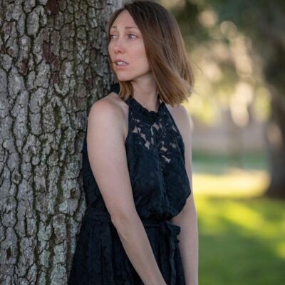 A woman in a black dress leaning against a tree