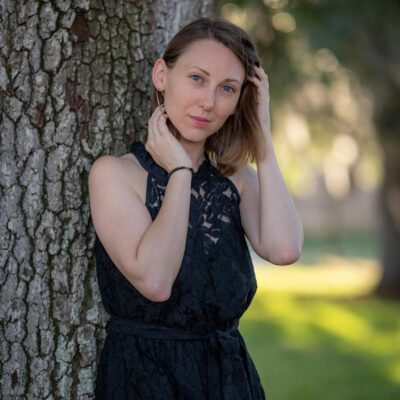 A woman in a black dress leaning against a tree