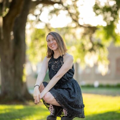A young woman in a black dress sits on a stump